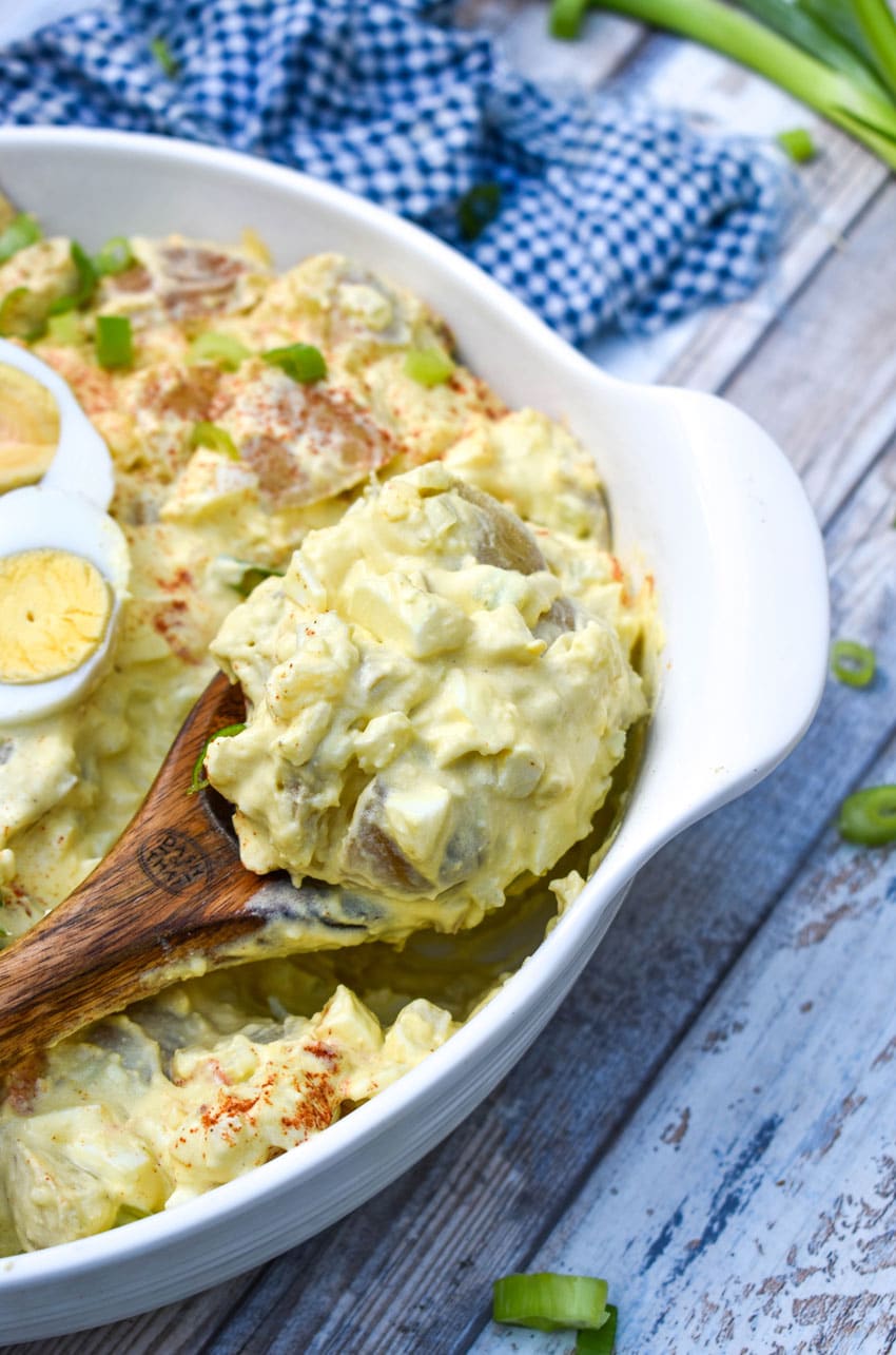 a wooden spoon scooping deviled egg potato salad out of a white serving bowl