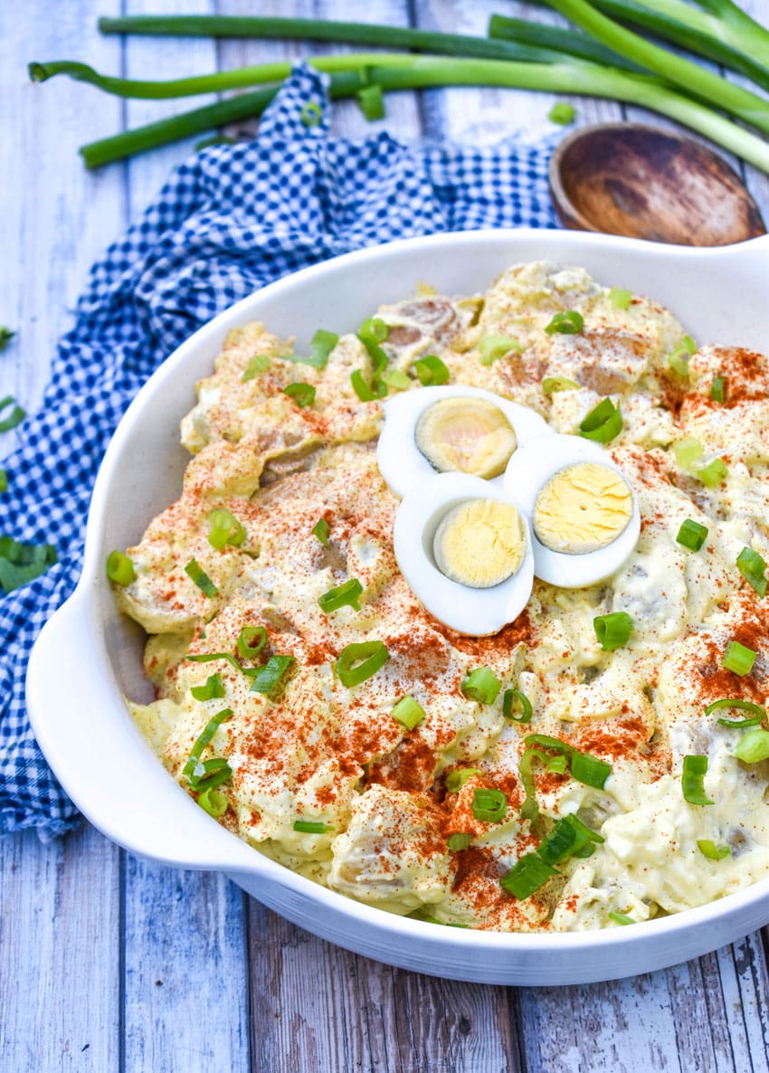 deviled egg potato salad in a white serving bowl topped with sliced green onions