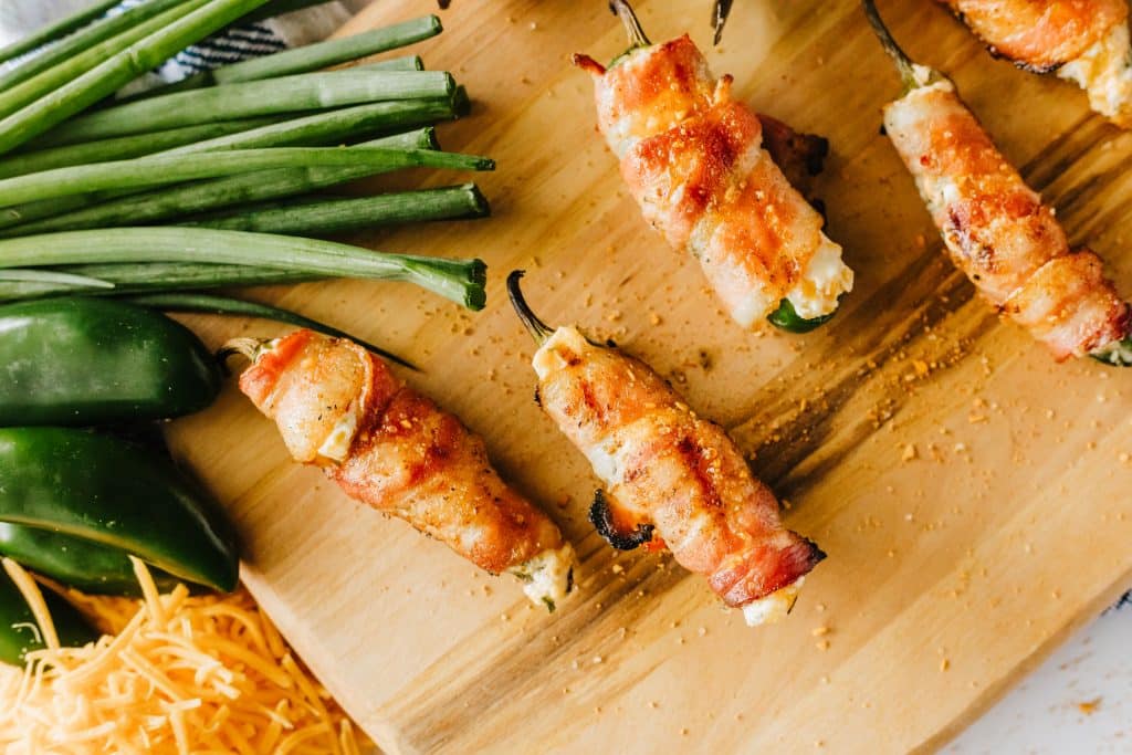 bacon wrapped grilled jalapeno poppers on a wooden cutting board