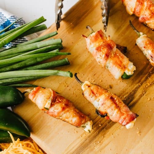bacon wrapped grilled jalapeno poppers on a wooden cutting board