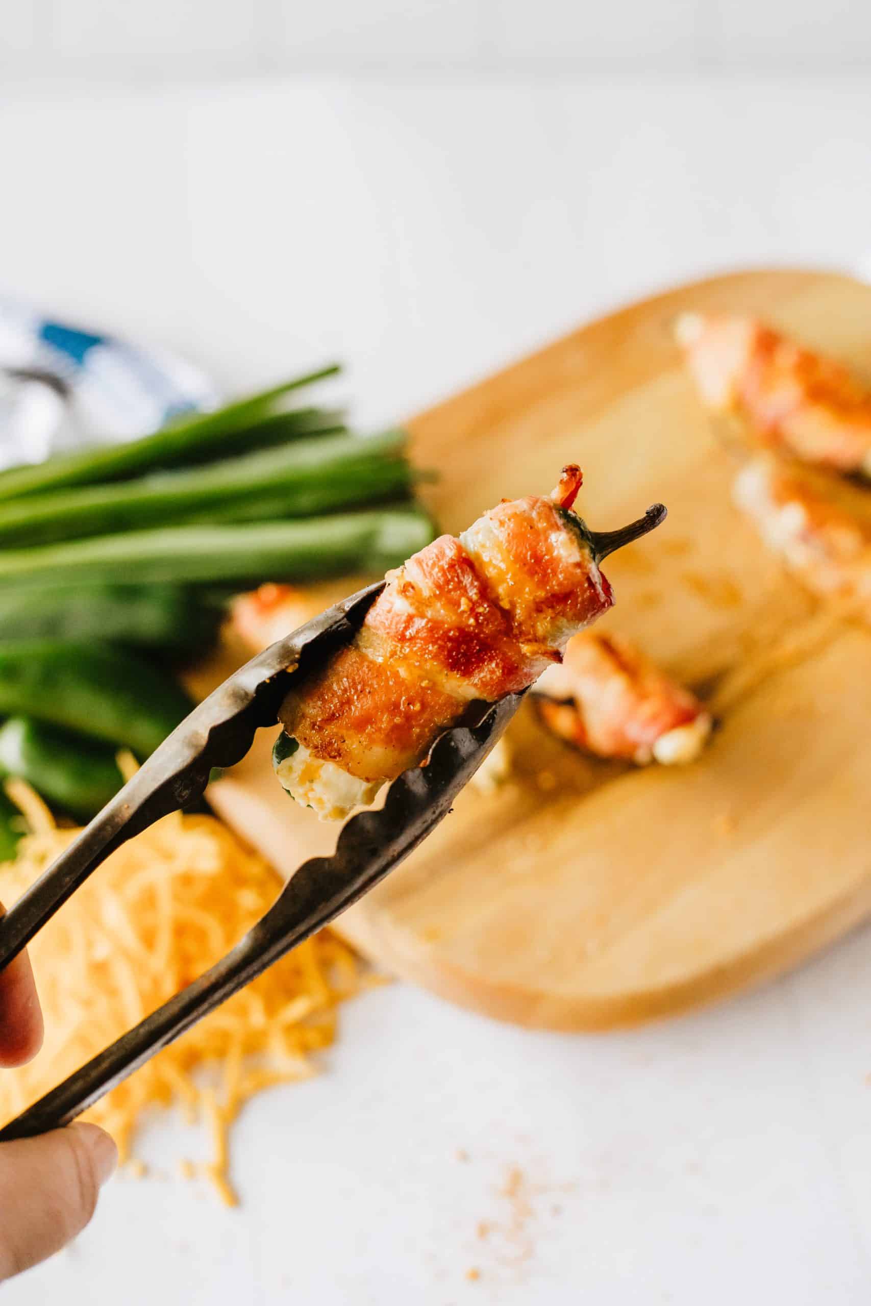 metal tongs holding up a bacon wrapped grilled jalapeno popper