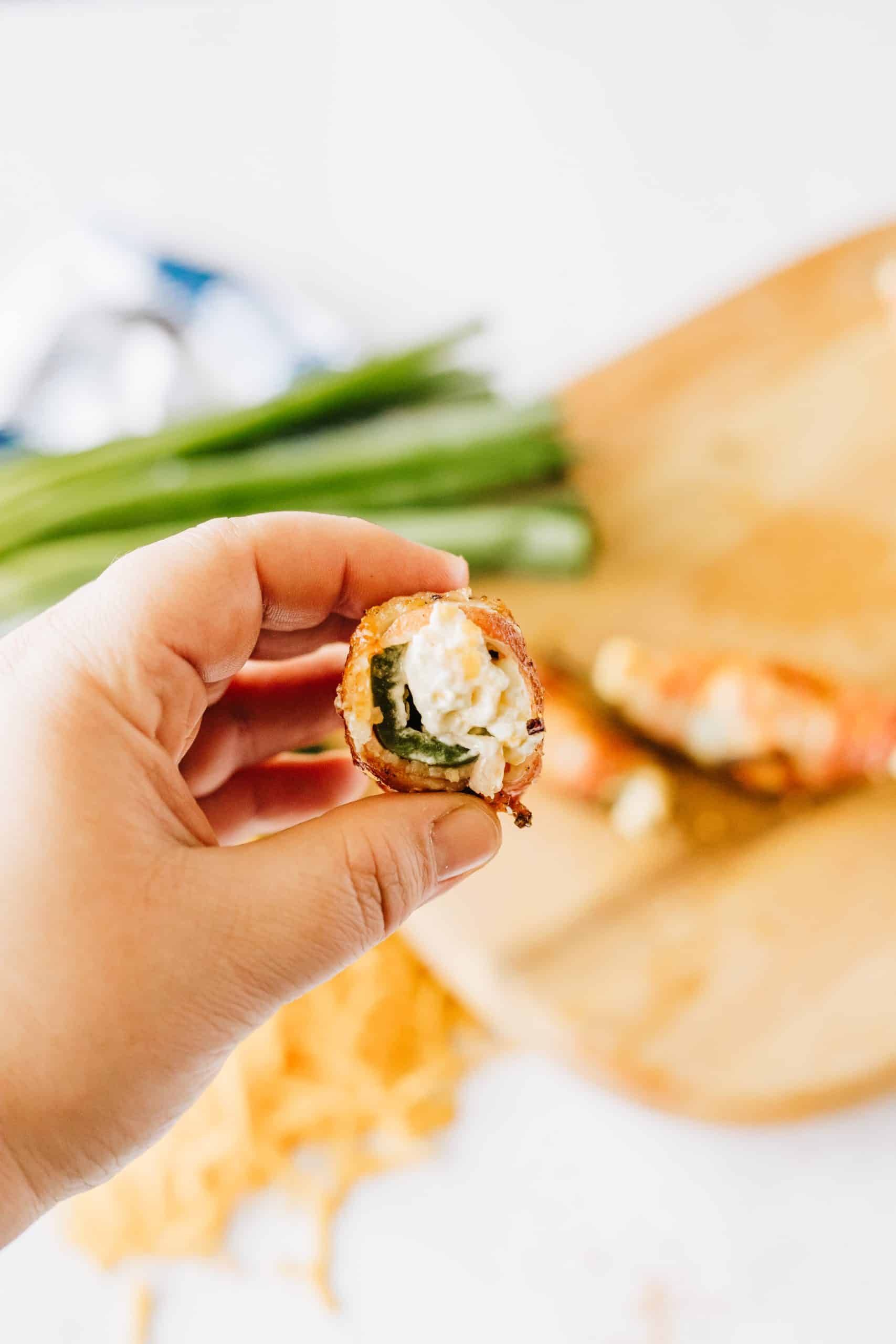 a hand holding up a half of a grilled jalapeno popper showing the creamy filling inside