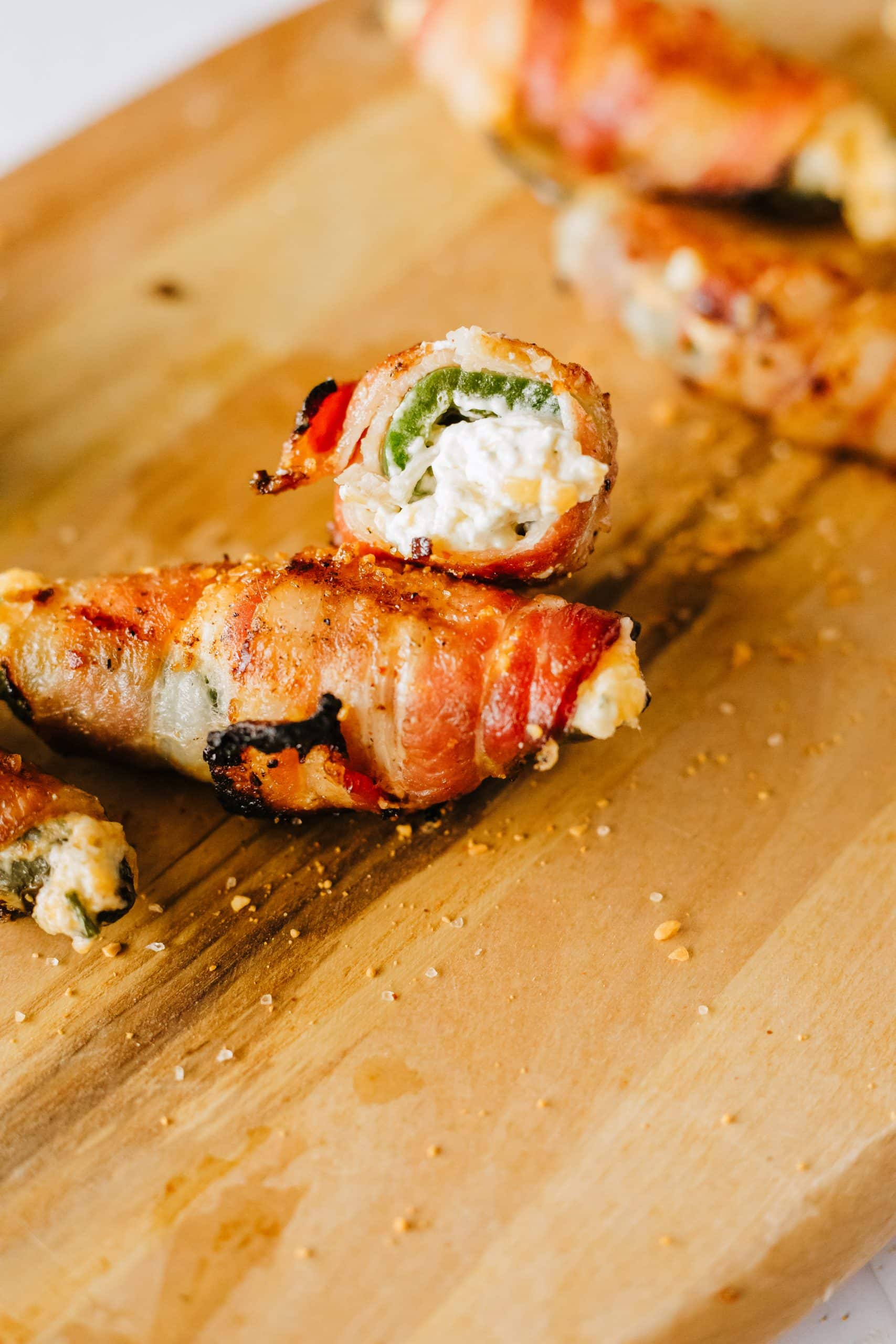 halved grilled jalapeno poppers on a wooden cutting board