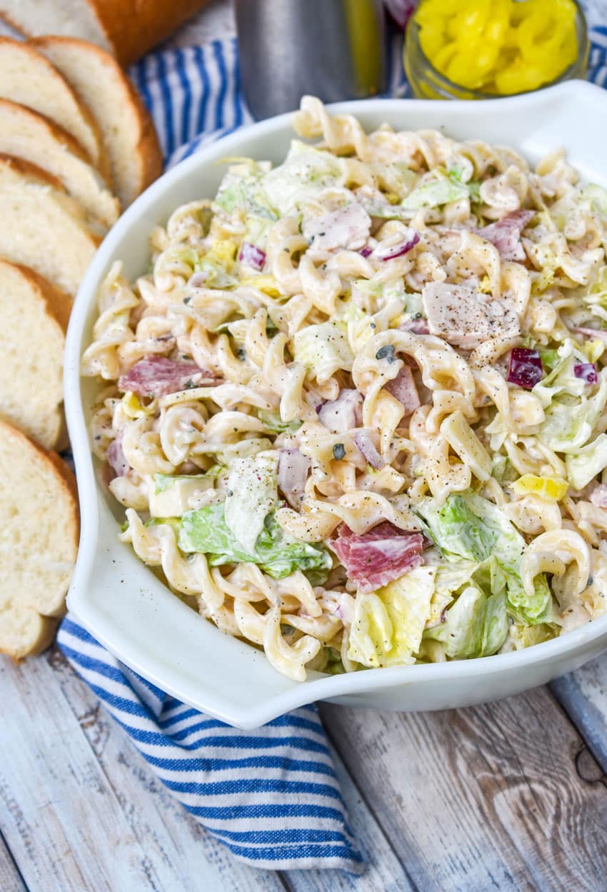 grinder sandwich pasta salad in a white serving bowl with a wooden spoon on the side