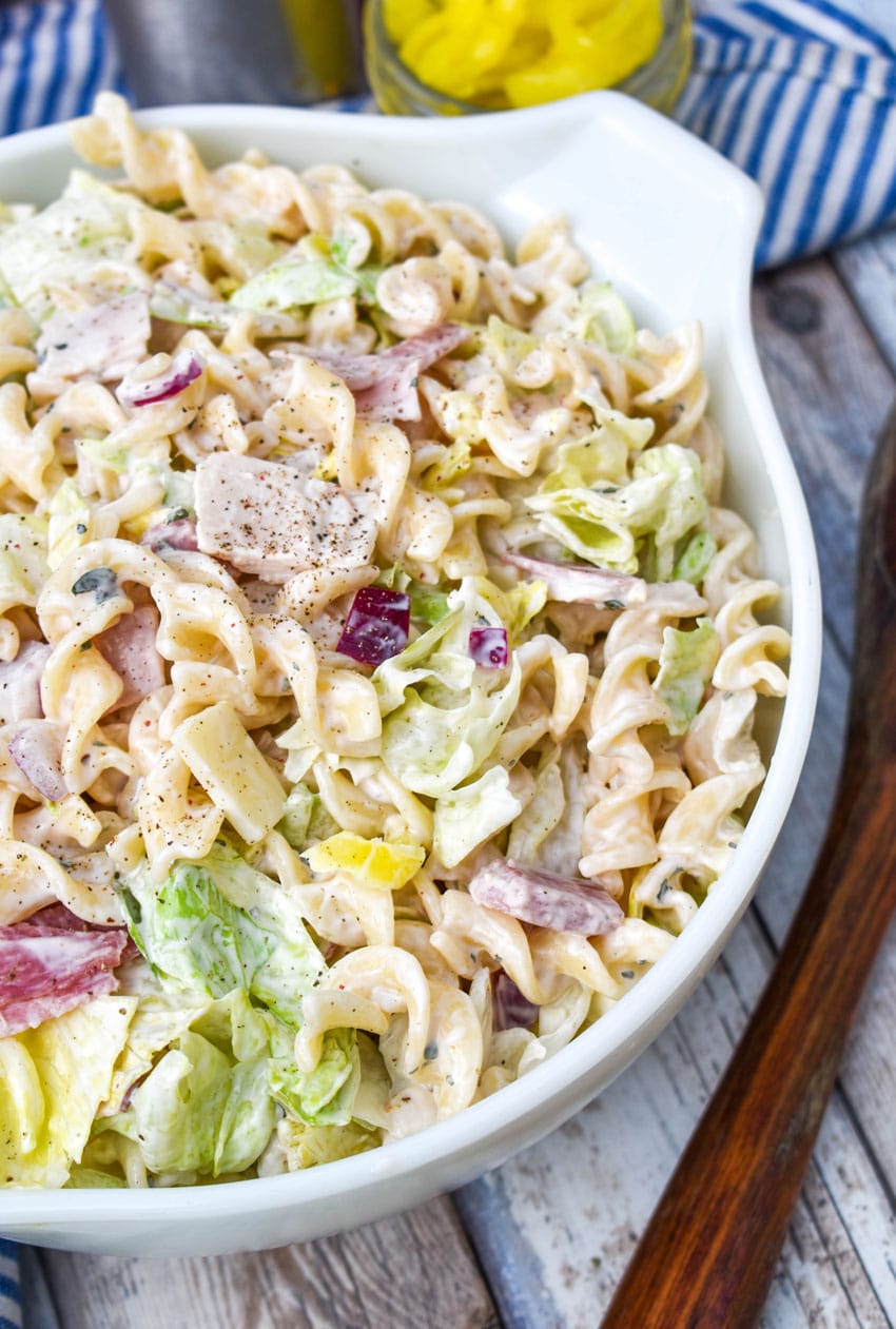grinder sandwich pasta salad in a white serving bowl with a wooden spoon on the side