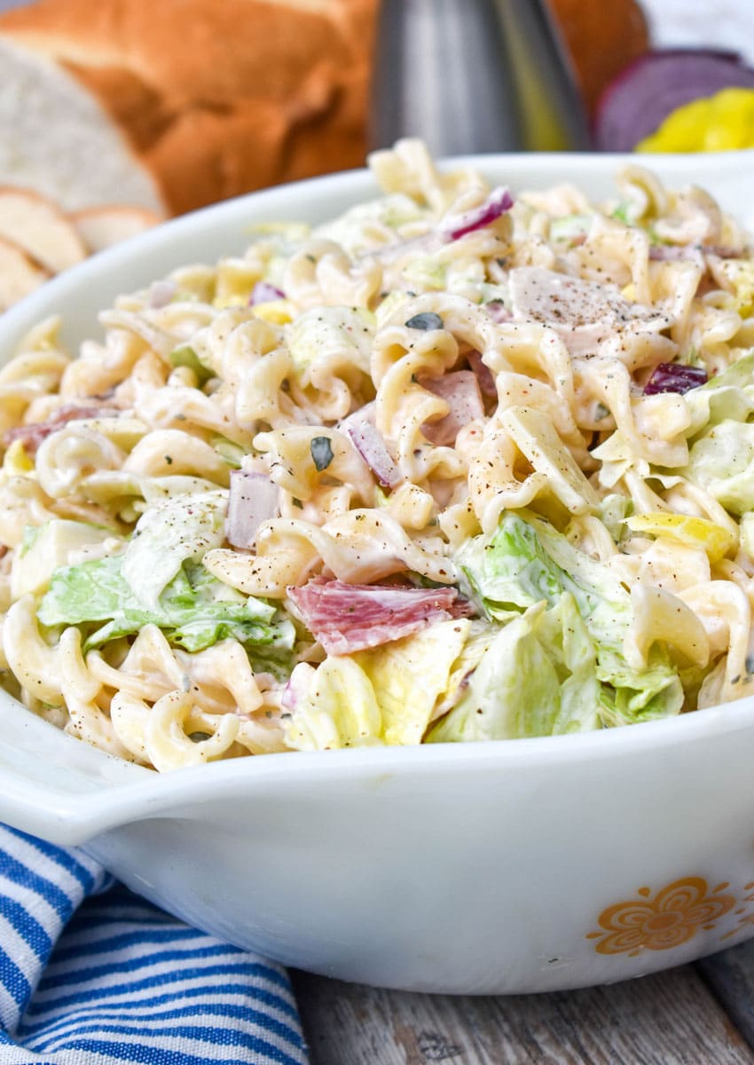 grinder sandwich pasta salad in a white serving bowl with a wooden spoon on the side