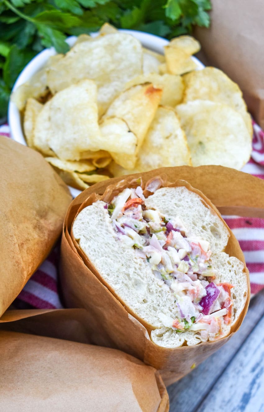 cut open Italian chopped sandwiches with a bowl of chips on the side