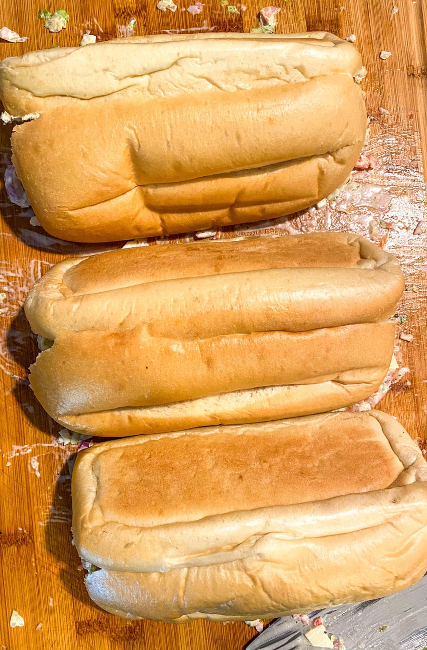 Italian chop chop sub mixture covered with hoagie rolls on a wooden cutting board
