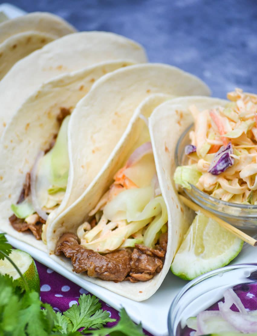 a row of korean steak tacos on a white serving platter