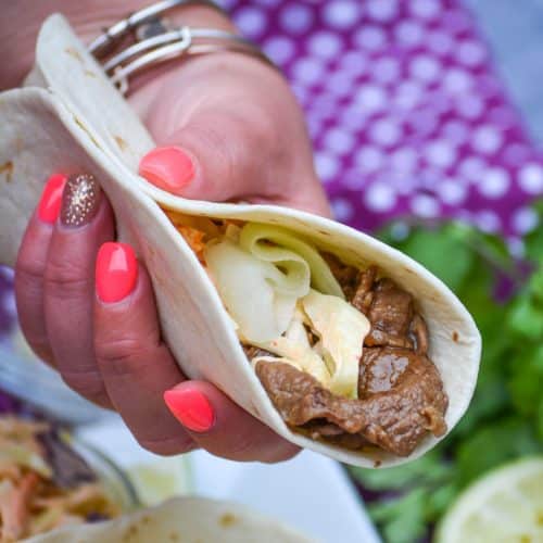 a hand holding up a korean stuffed taco in a flour tortilla