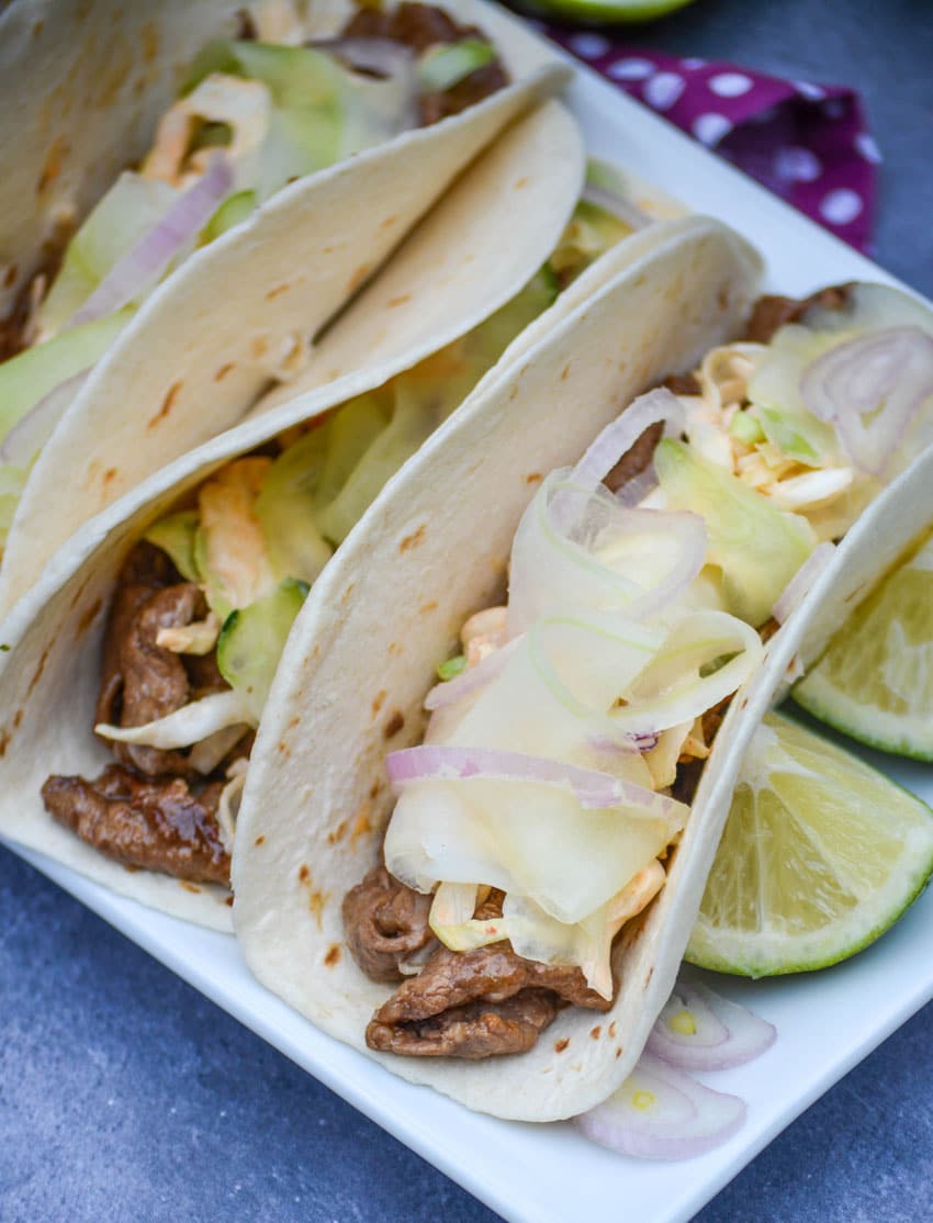 a row of korean steak tacos on a white serving platter