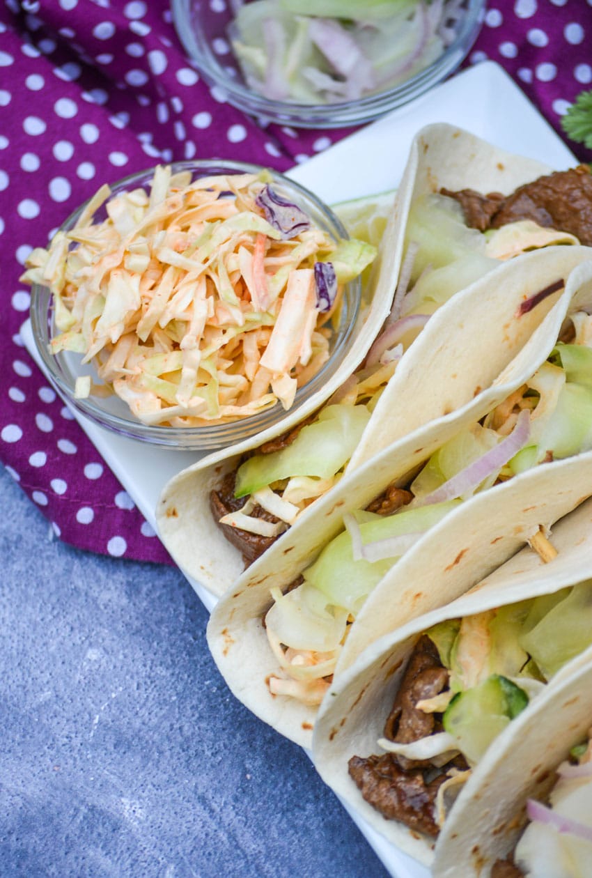 spicy Asian slaw in a small glass bowl on a platter of asian steak tacos