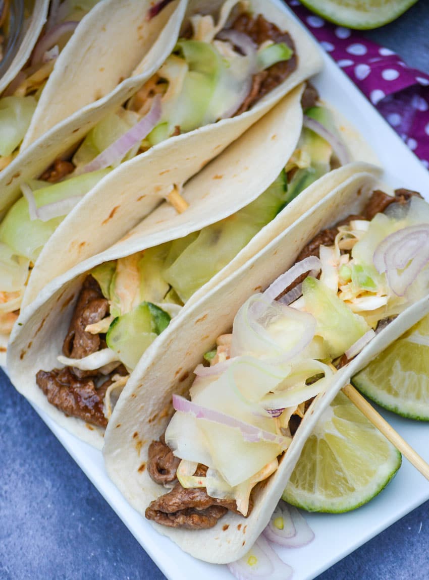 a row of korean steak tacos on a white serving platter
