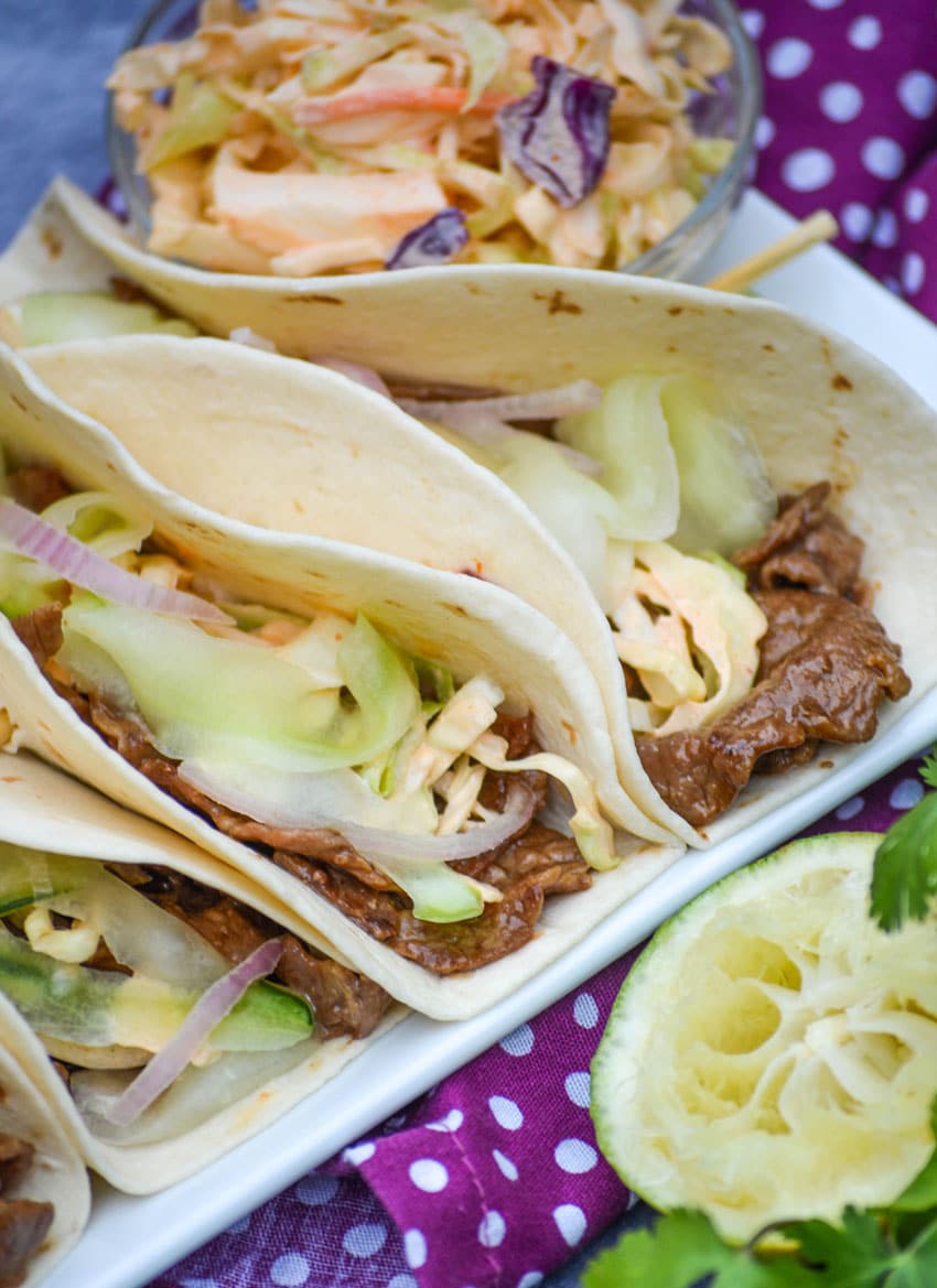 a row of korean steak tacos on a white serving platter