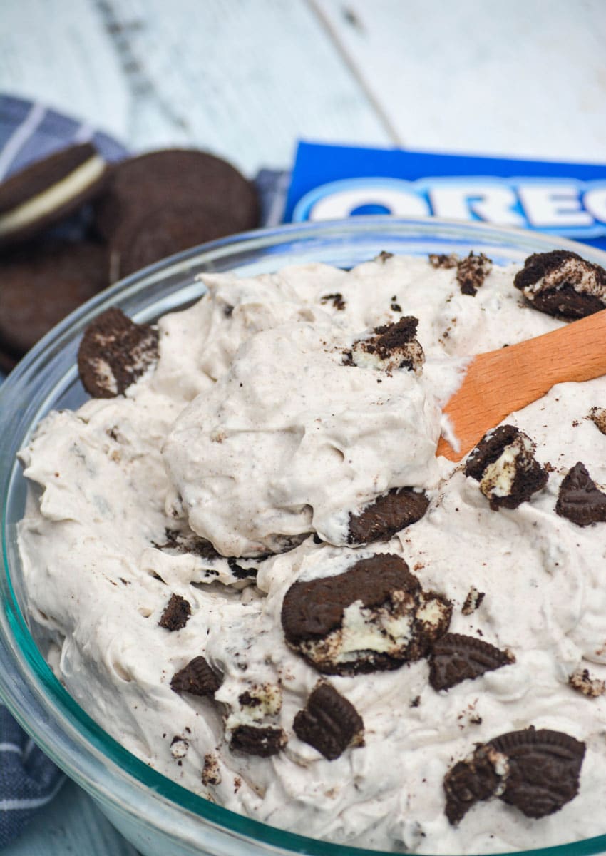 a wooden spoon stuck in a glass bowl filled with oreo cookie salad