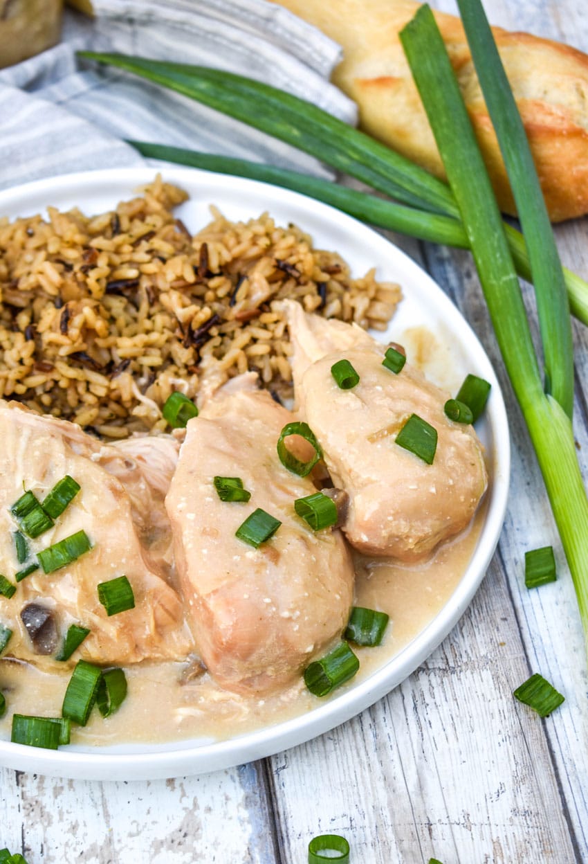 slow cooker sour cream and onion chicken topped with green onions and potato chips on a white plate with rice on the side