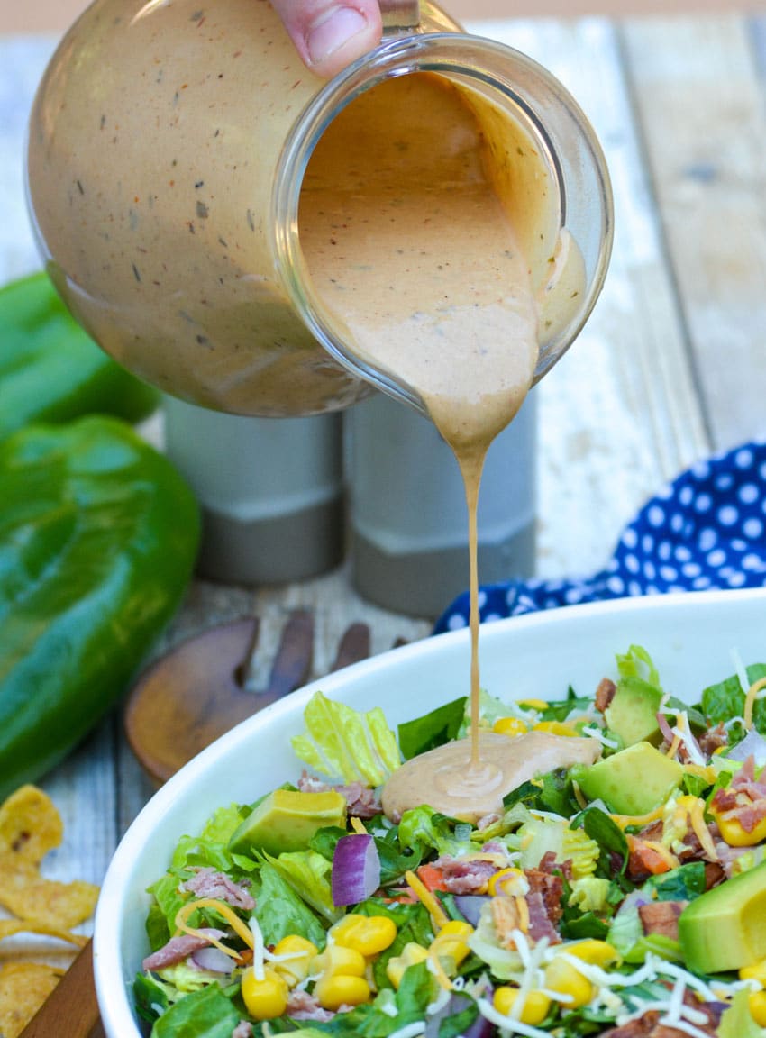 barbecue ranch dressing being poured over a chopped salad recipe