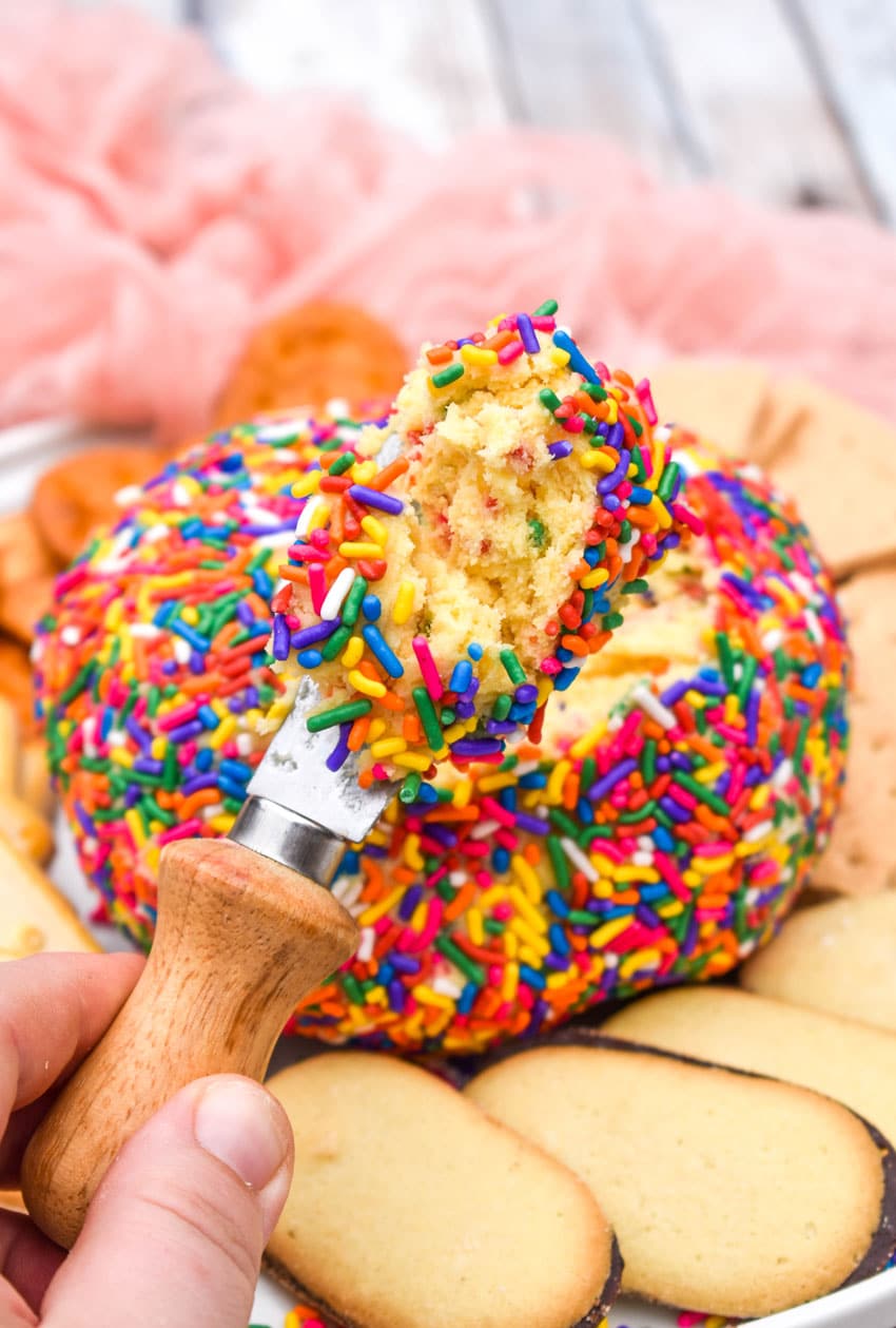 a wooden handled spreader holding up a scoop of cake batter cheese ball