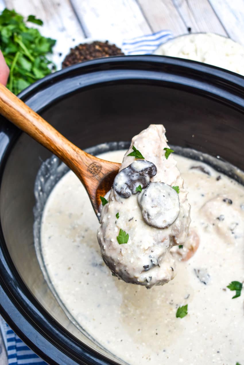a wooden spoon in a black crock filled with Slow Cooker Peppercorn Chicken with Mushrooms