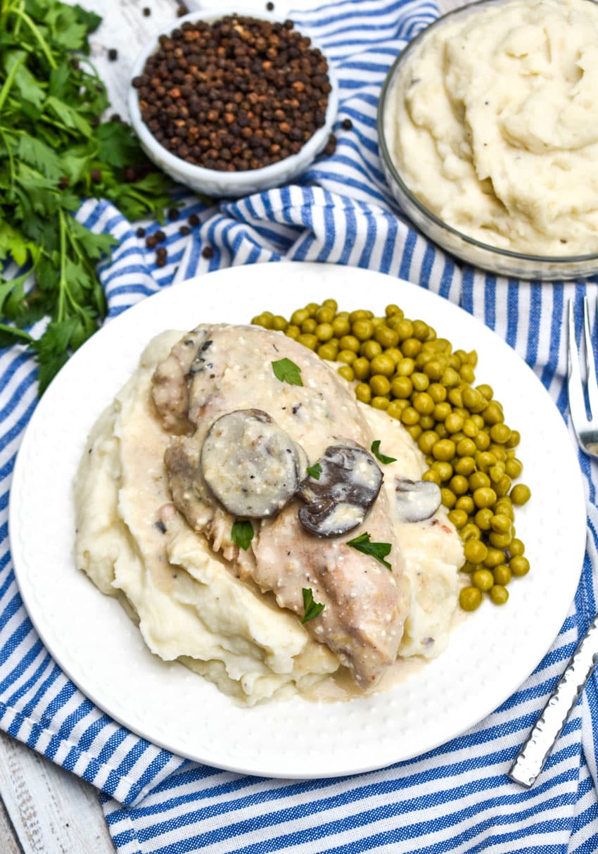 crockpot parmesan peppercorn chicken with mushrooms over mashed potatoes on a white plate
