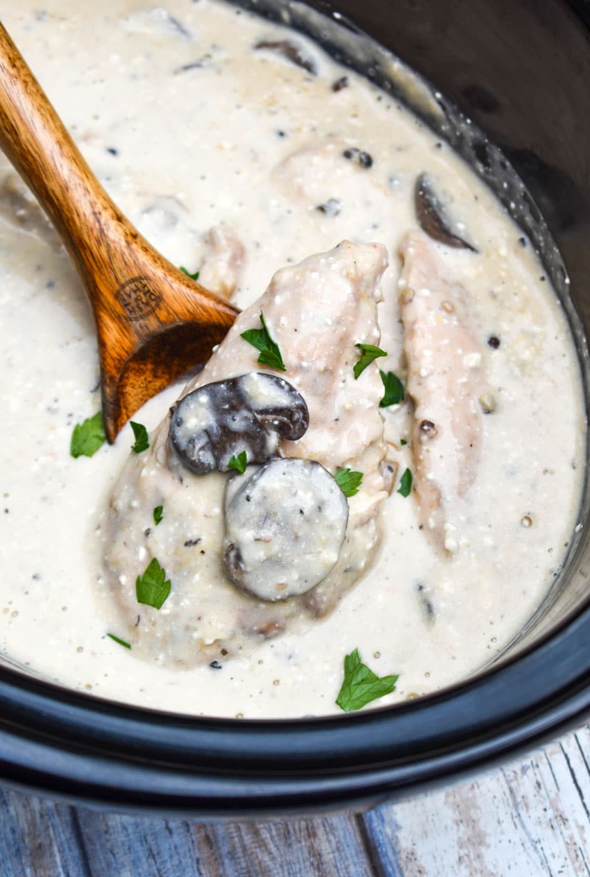 a wooden spoon in a black crock filled with Slow Cooker Peppercorn Chicken with Mushrooms