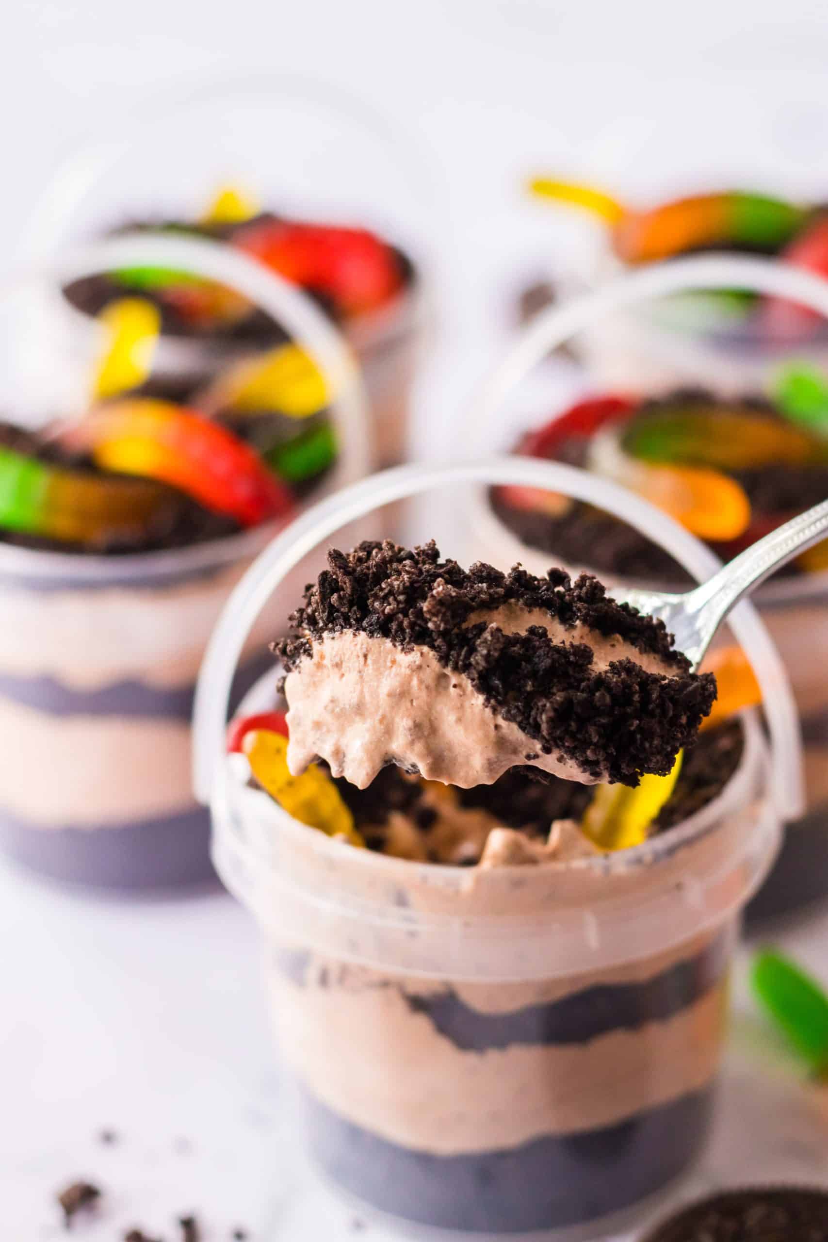 a spoon scooping oreo dirt pudding out of a small plastic tub