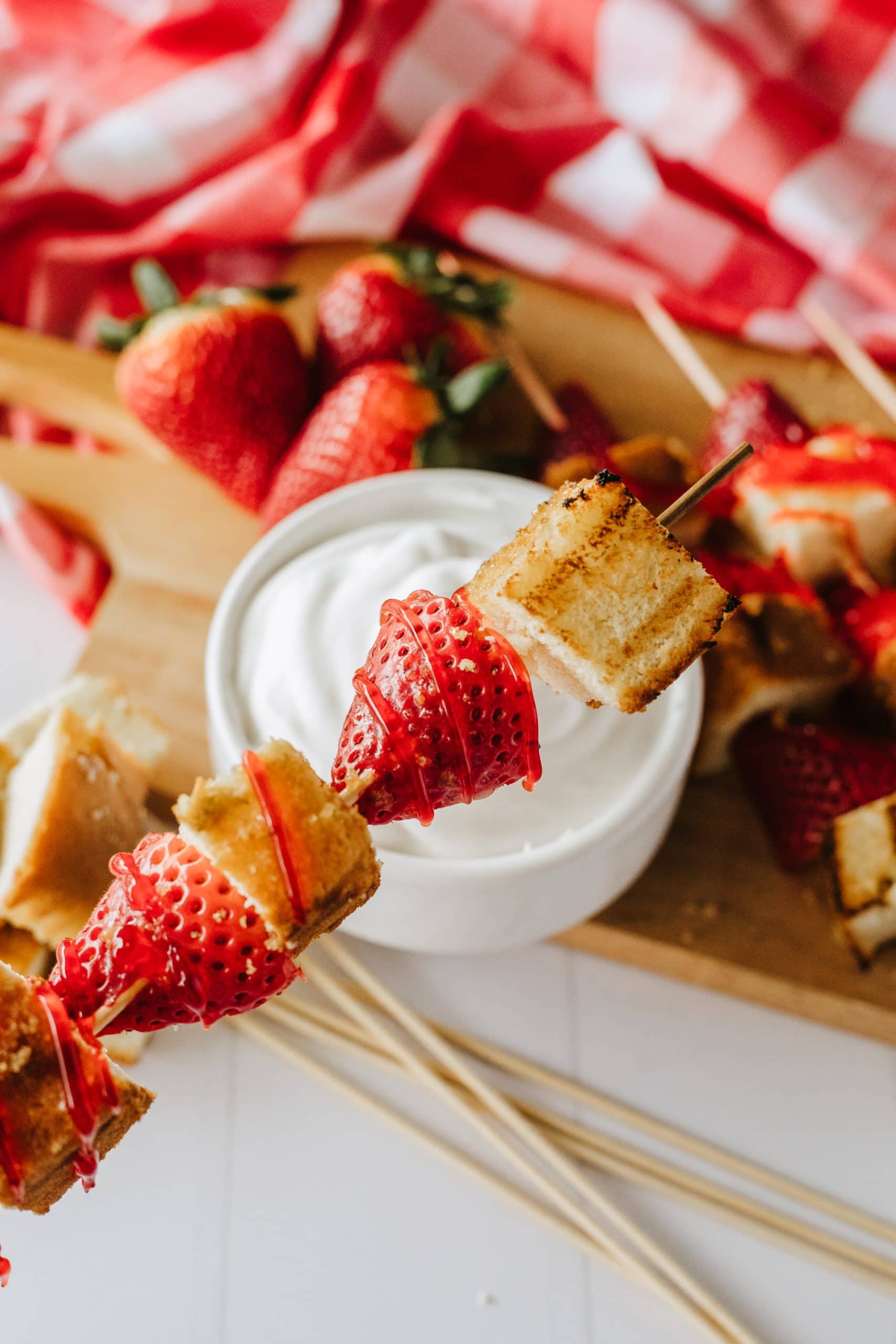 a grilled strawberry shortcake skewer held over a bowl of whipped topping