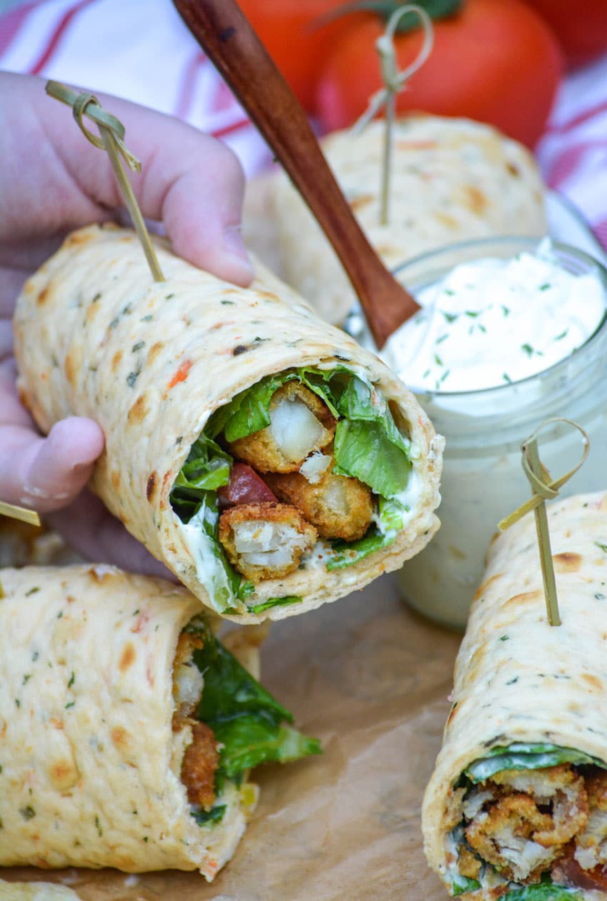 a hand holding up half of a simple wrap stuffed with fish sticks