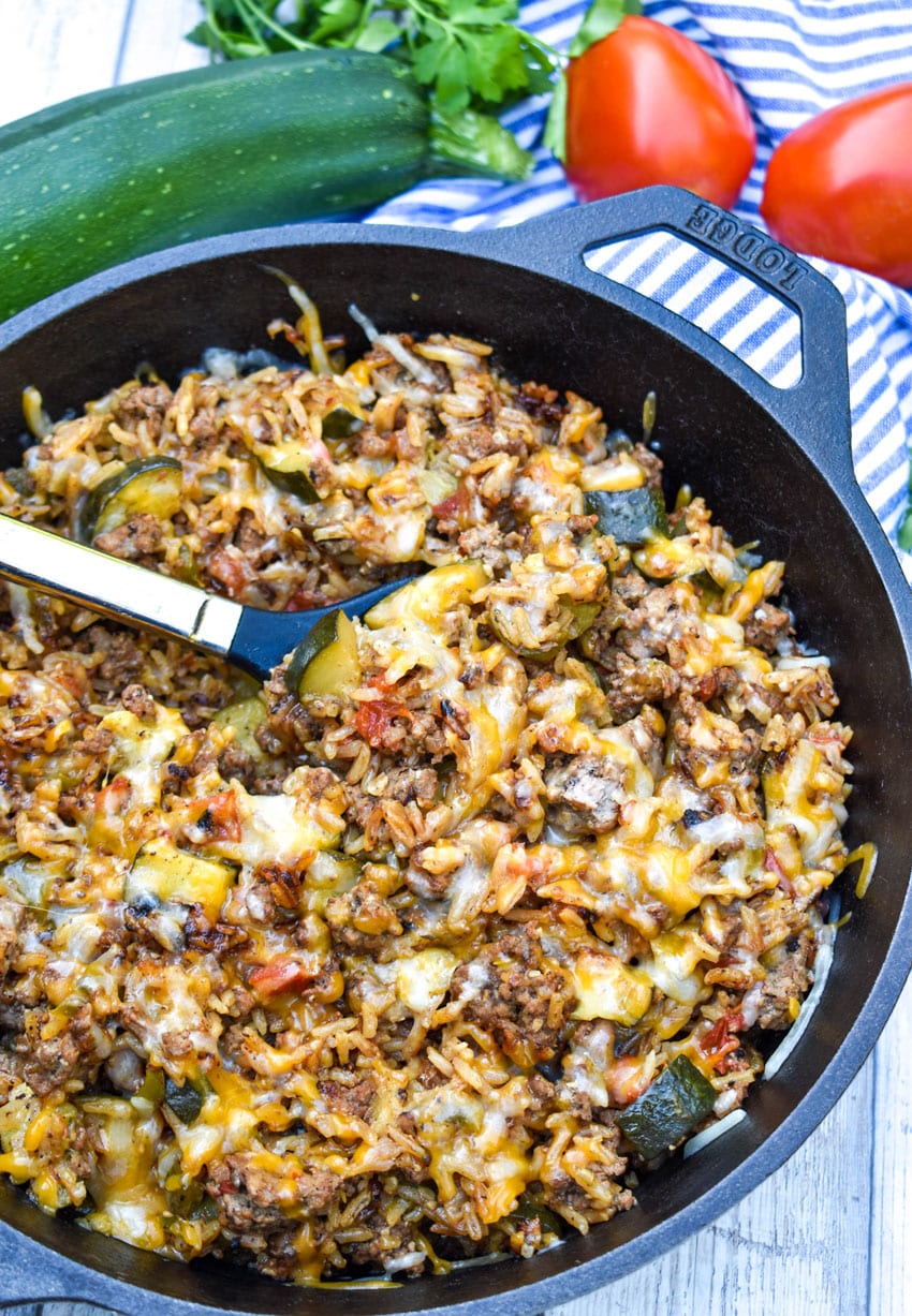 a spoon stuck in a cast iron skillet filled with ground beef zucchini and rice