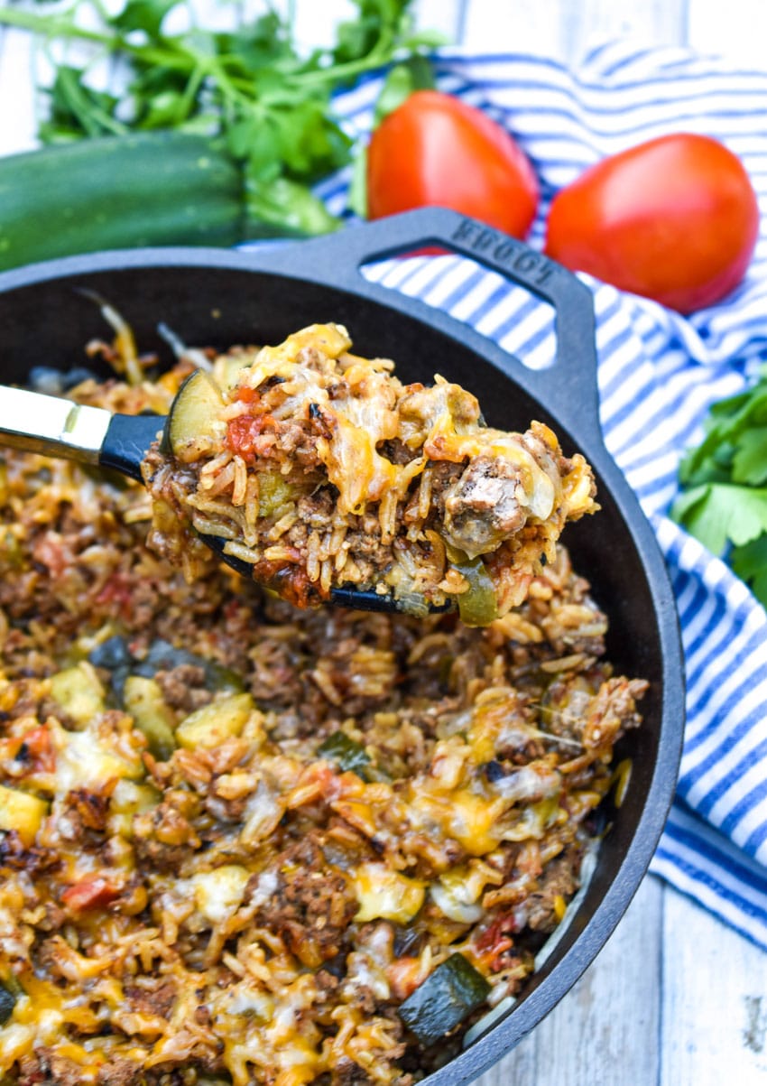a serving spoon holding a scoop of ground beef zucchini and rice above a cast iron skillet