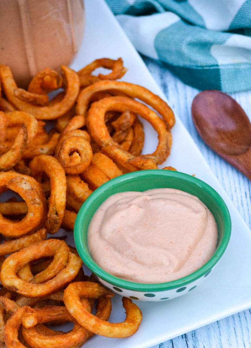 a small green bowl of comeback sauce on a white platter surrounded by crisp curly fries