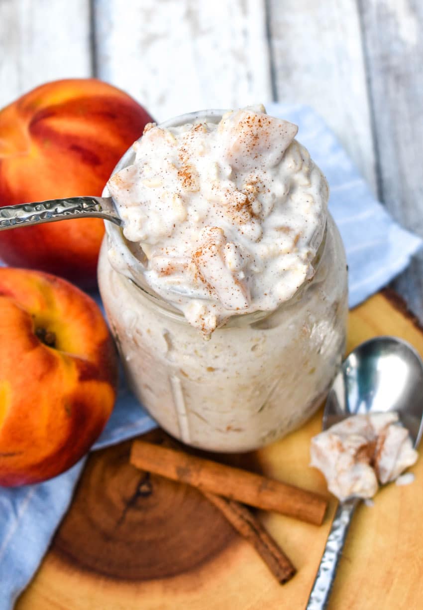 a silver spoon stuck in a glass jar filled with creamy peach overnight oatmeal