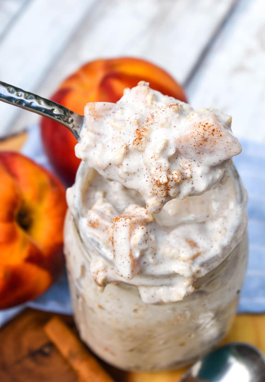 a silver spoon holding up a scoop of peaches and cream overnight oats