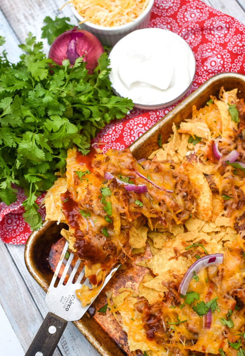 a spatula lifting nachos with barbecue pork off a sheet pan