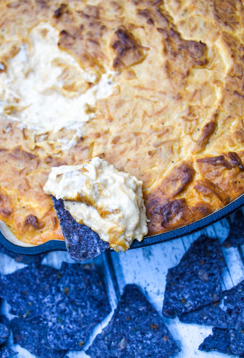 a blue corn chip covered with creamy buffalo chicken dip resting on the edge of a skillet