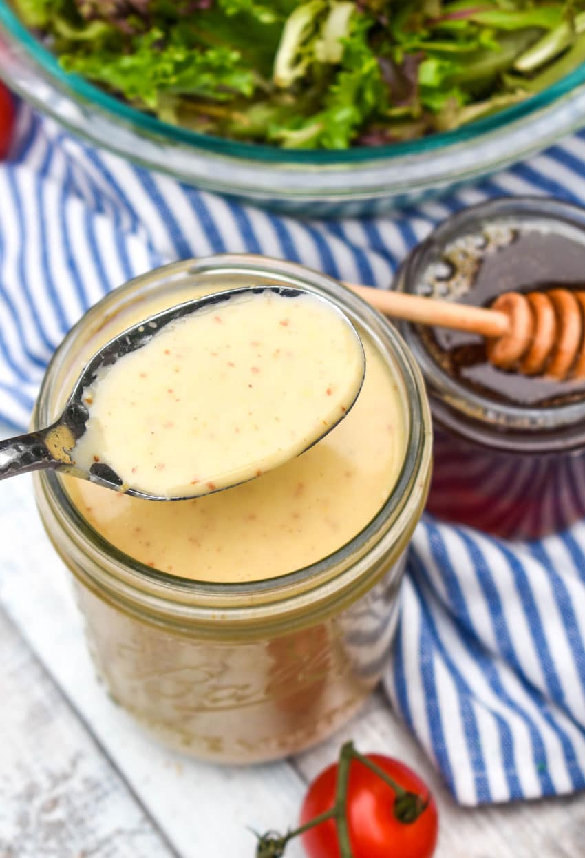 a silver spoon scooping honey mustard vinaigrette out of a glass jar