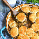 a wooden spoon in a blue skillet filled with beef pot pie with biscuits