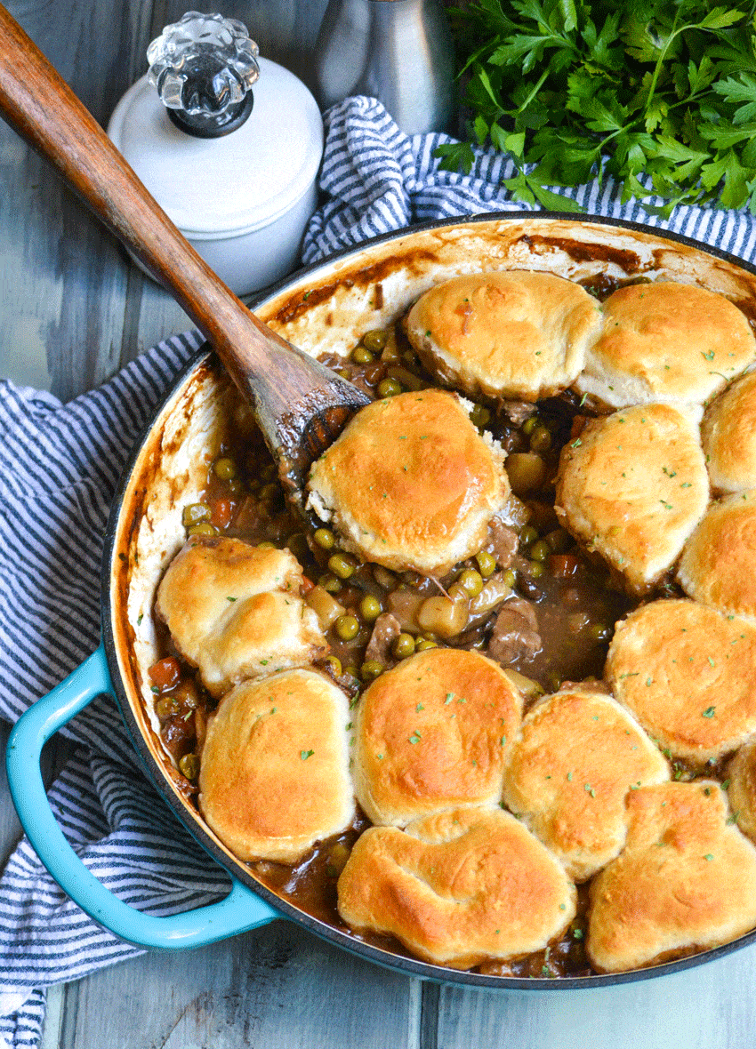 a wooden spoon in a blue skillet filled with beef pot pie with biscuits