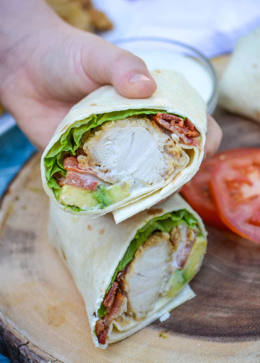 a hand holding up half of a california chicken club wrap with avocado