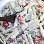 a wooden spoon stuck in a bowl of creamy Greek pasta salad