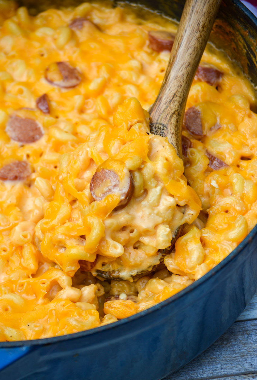 a wooden spoon scooping firehouse mac and cheese with hot dogs out of a large blue pot