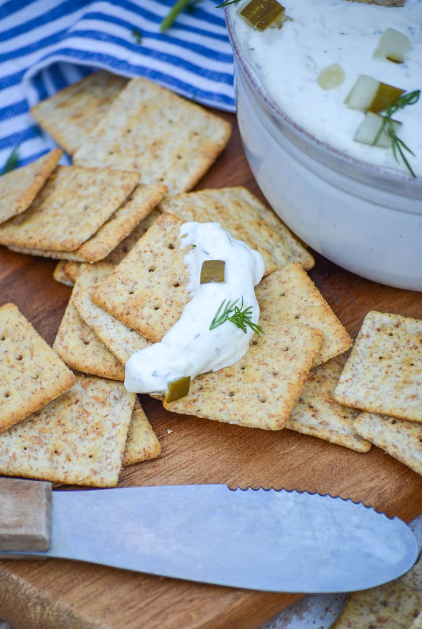 creamy dill pickle dip on a cracker on a wooden cutting board