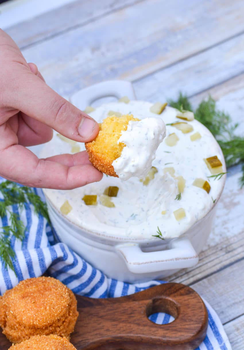 a broken hush puppie dipped in a bowl of pickle dip