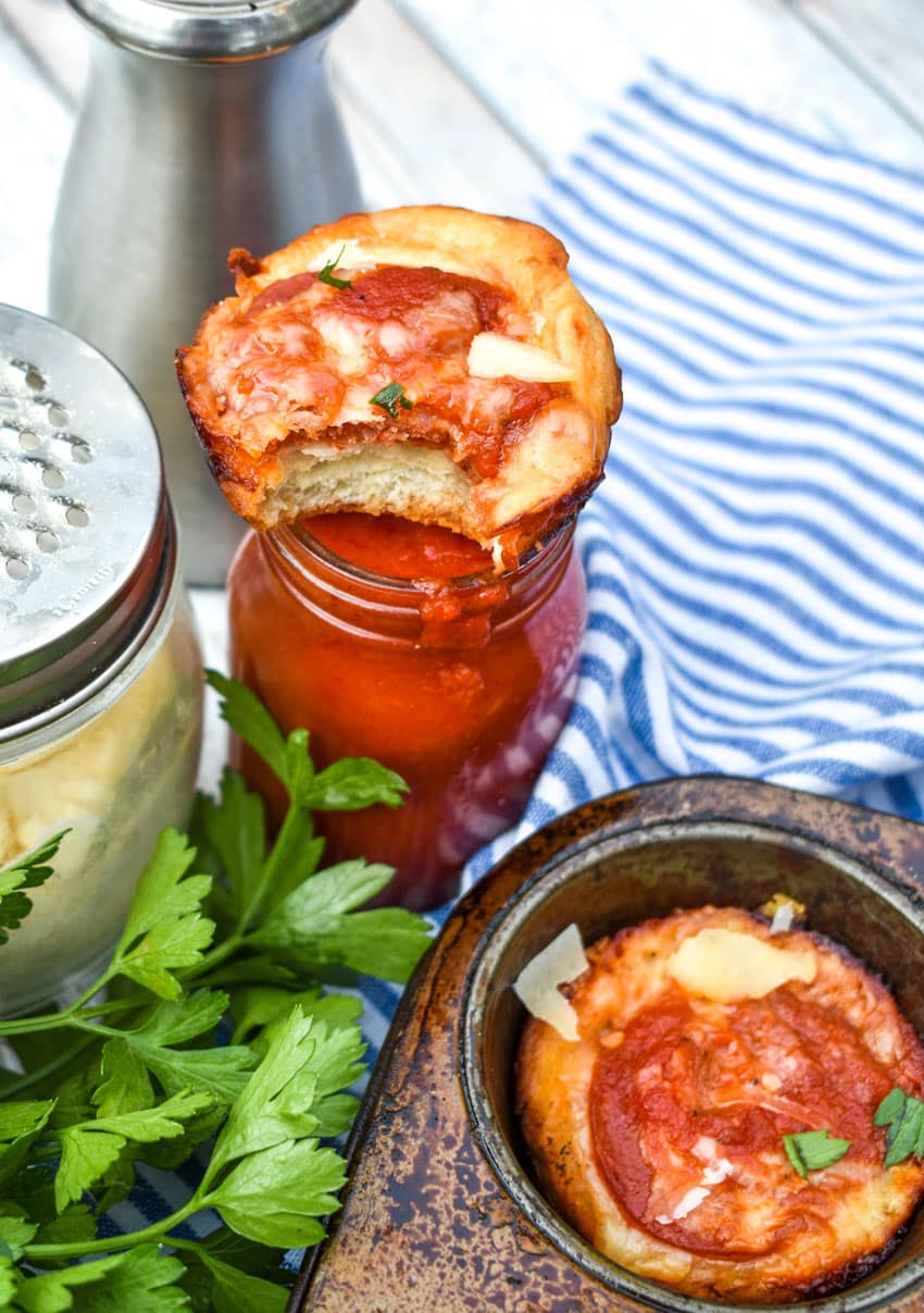 a bitten mini deep dish pizza bite resting on the edge of a glass jar filled with pasta sauce