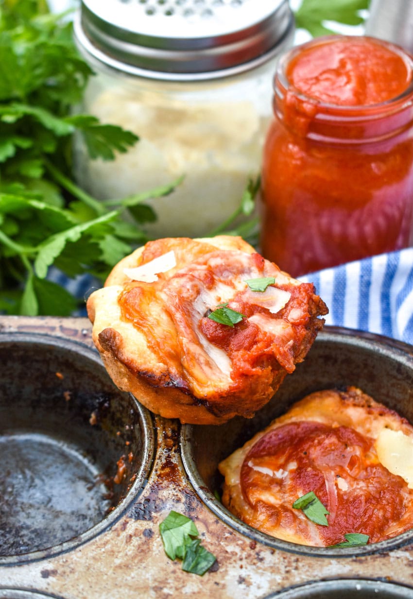 mini deep dish pizzas stacked on the edge of a metal muffin tin