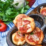 mini deep dish pizzas stacked on the edge of a metal muffin tin