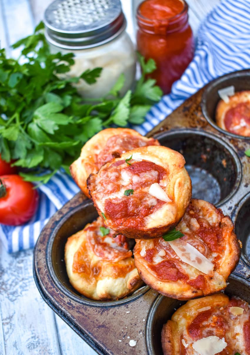 mini deep dish pizzas stacked on the edge of a metal muffin tin