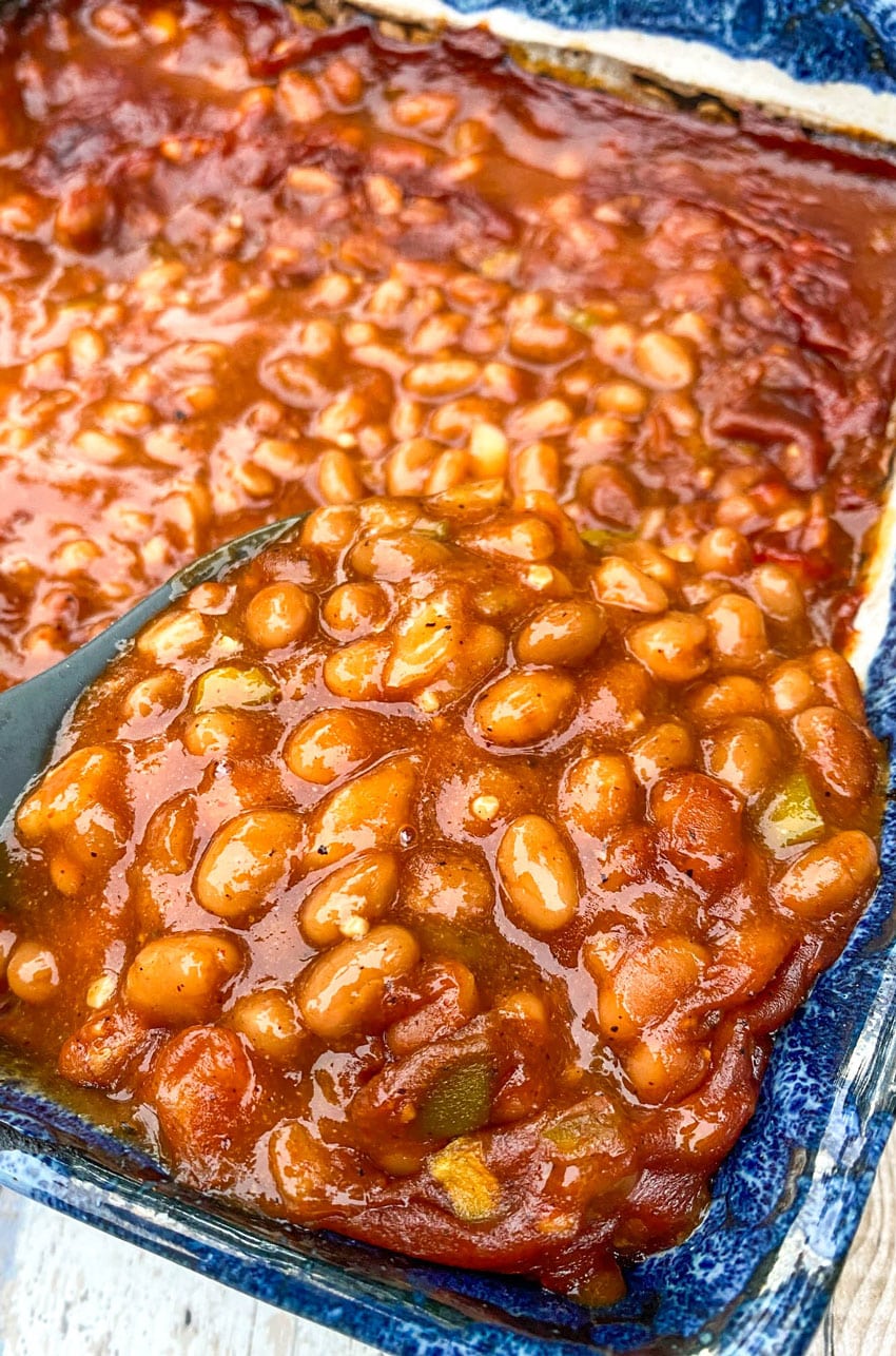 a serving spoon stuck in a cast iron dish filled with smoked baked beans