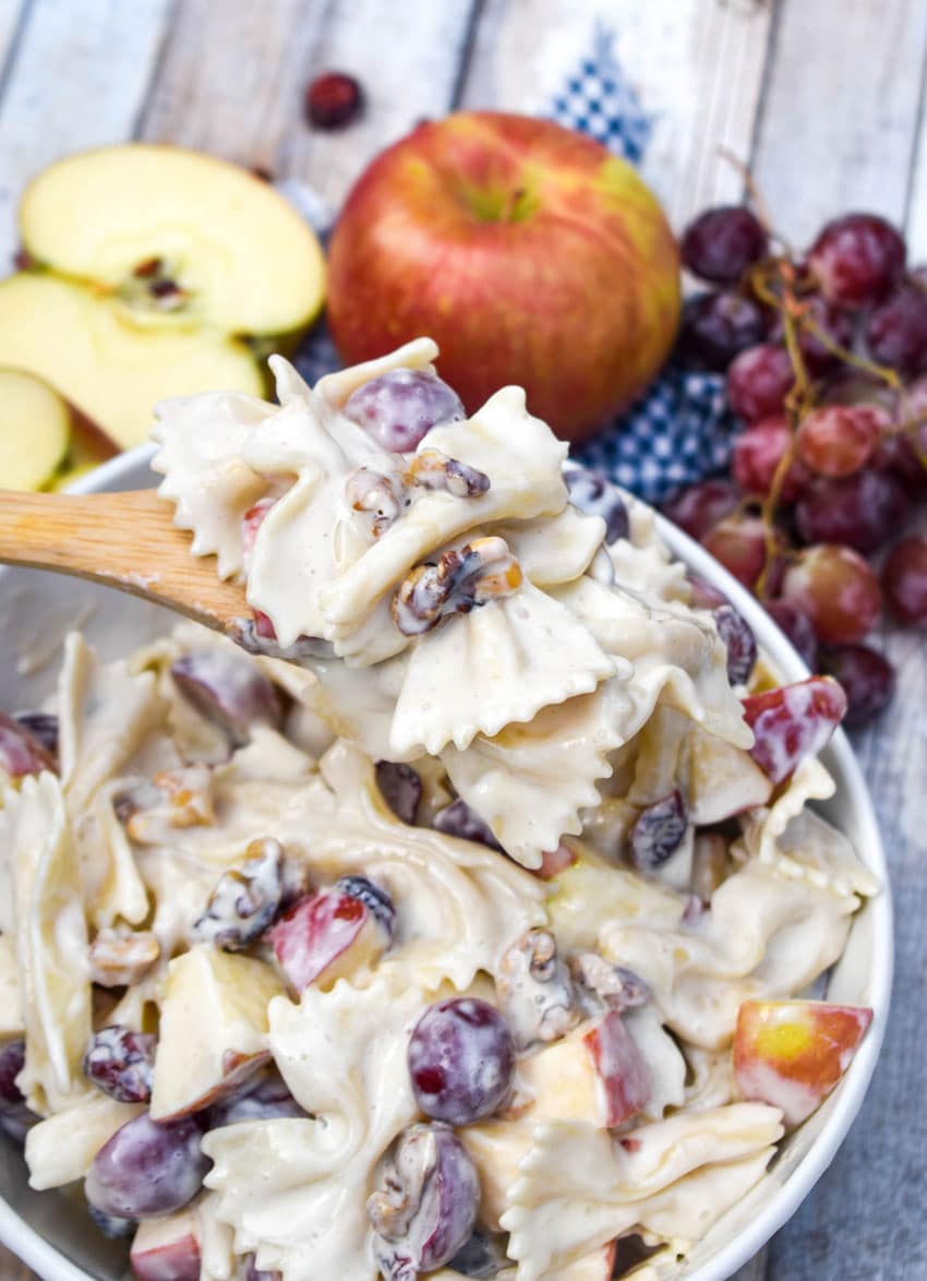 a wooden spoon holding up a scoop of creamy pasta salad with fruit recipe