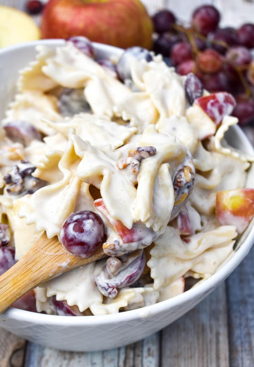 a wooden bowl in a white bowl filled with a creamy pasta with fruit recipe